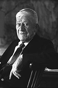 Schwarz-Weiß-Porträt eines gealterten Oskar Kokoschka; er sitzt lächelnd in einem Stuhl und blickt in die Kamera.